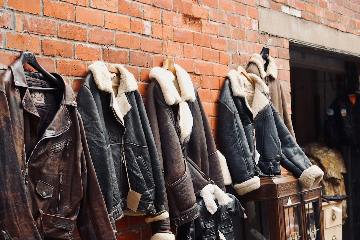 Leather and shearling jackets hanging on a red brick wall outside a workshop