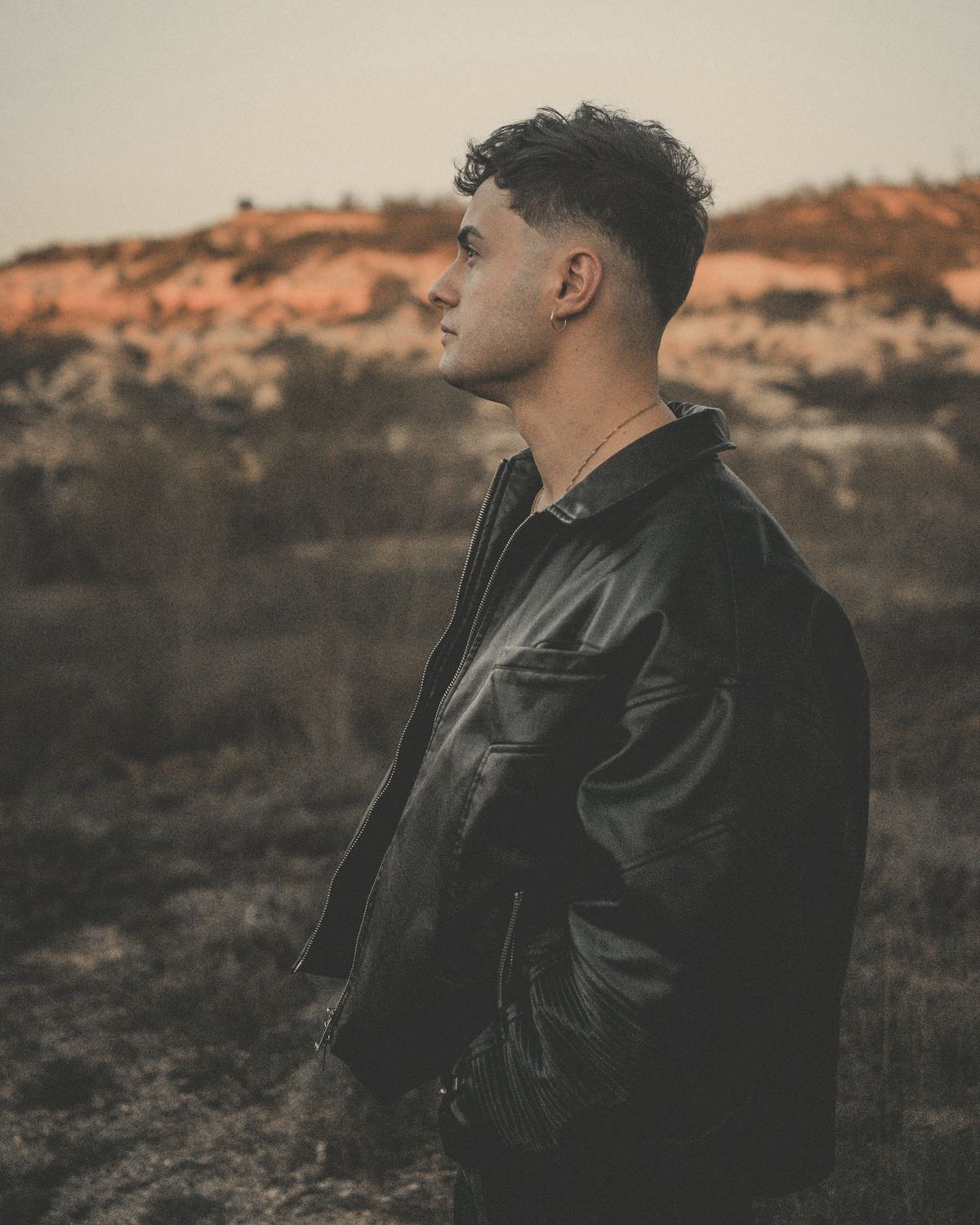 Man in a black leather blouson in profile against red-earth hills