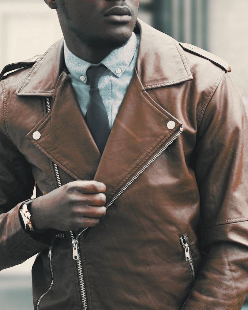 Cognac-brown leather biker jacket with snap lapels and a silver zip, worn with a blue shirt and dark tie