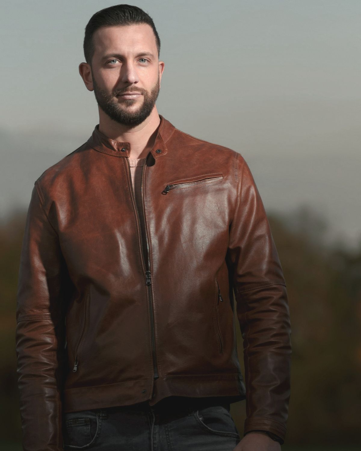 Man in a cognac leather café racer jacket with a snap collar and zip chest pocket