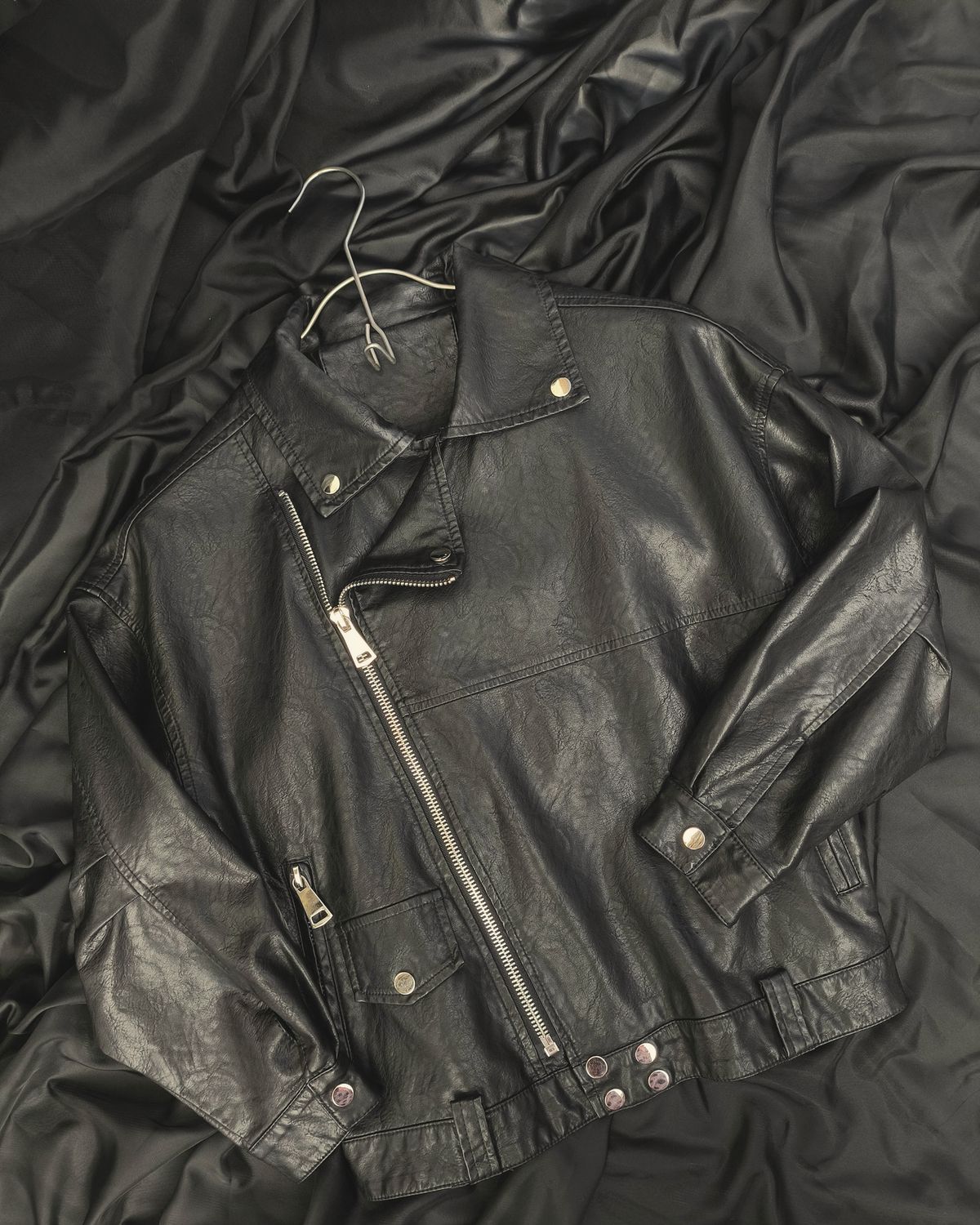 Black leather biker jacket laid flat with a metal hanger for scale