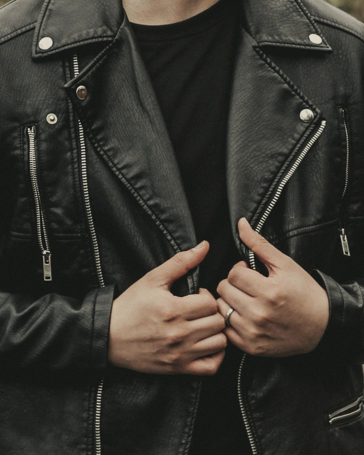 Hands holding open a black leather biker jacket, with snap lapels and silver zips