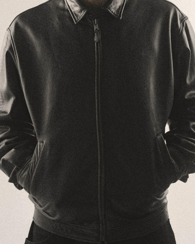 Black collared leather jacket with a centre zip, worn with hands in the pockets