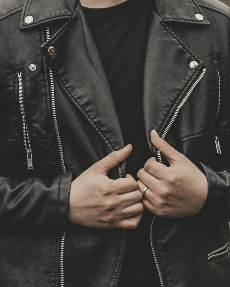 Close view of a black biker jacket with silver studs and zips, hands holding the lapels