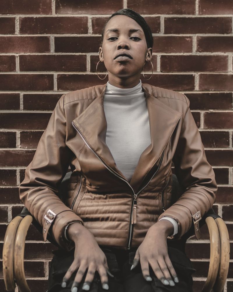 A customer seated against a brick wall in her cognac leather jacket