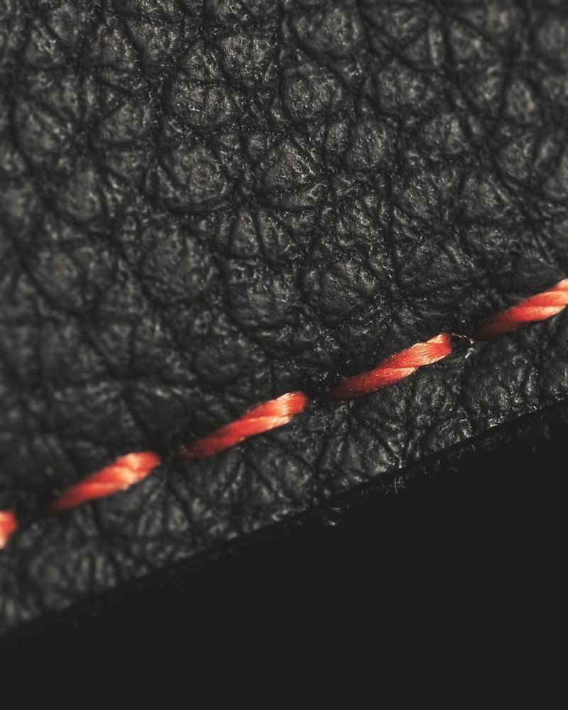 Close-up of orange stitching along a seam of black pebbled leather