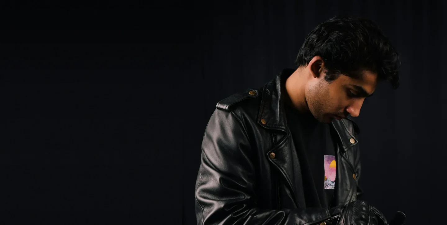 Man in a black leather biker jacket with brass snaps, photographed in a dark studio