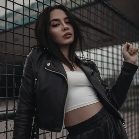 Customer in a cropped black biker jacket, leaning on a wire fence